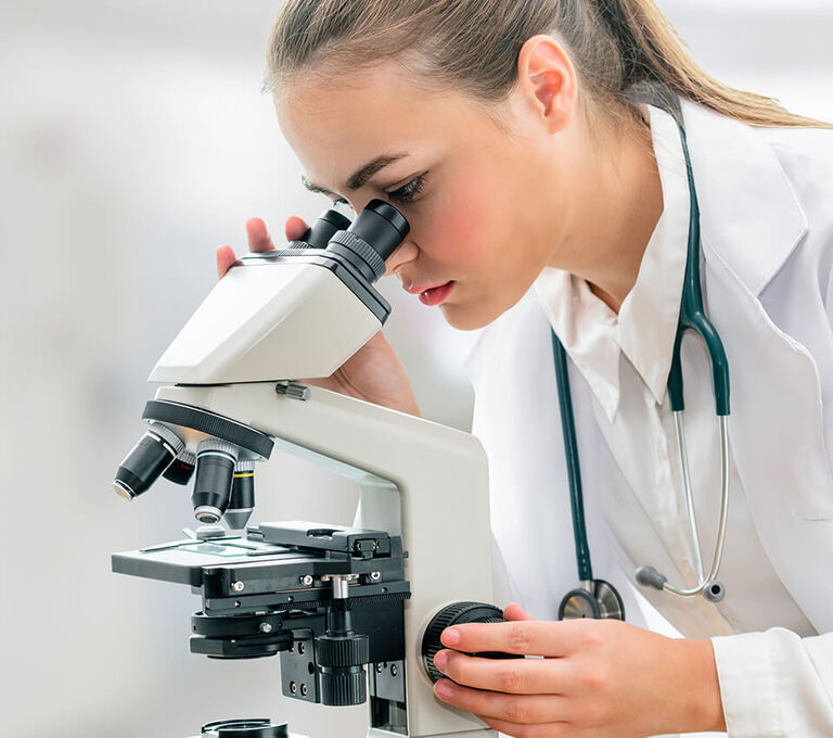 Dottoressa che fa' ricerca guardando attraverso un microscopio scientifico