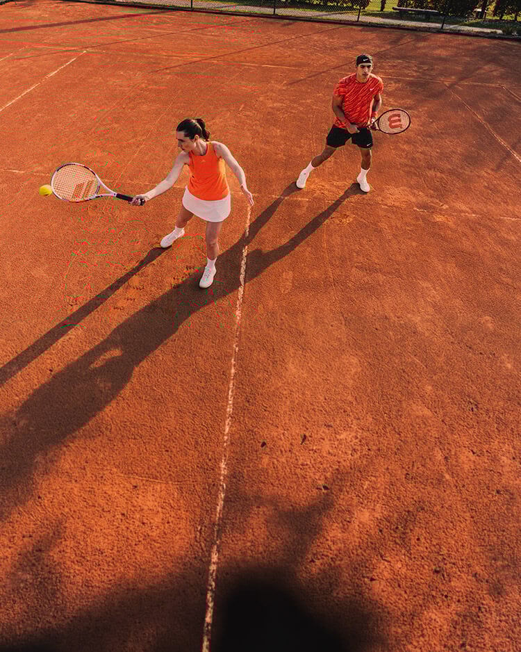Ragazzo e ragazza che giocano a tennis in campo di sabbia rossa