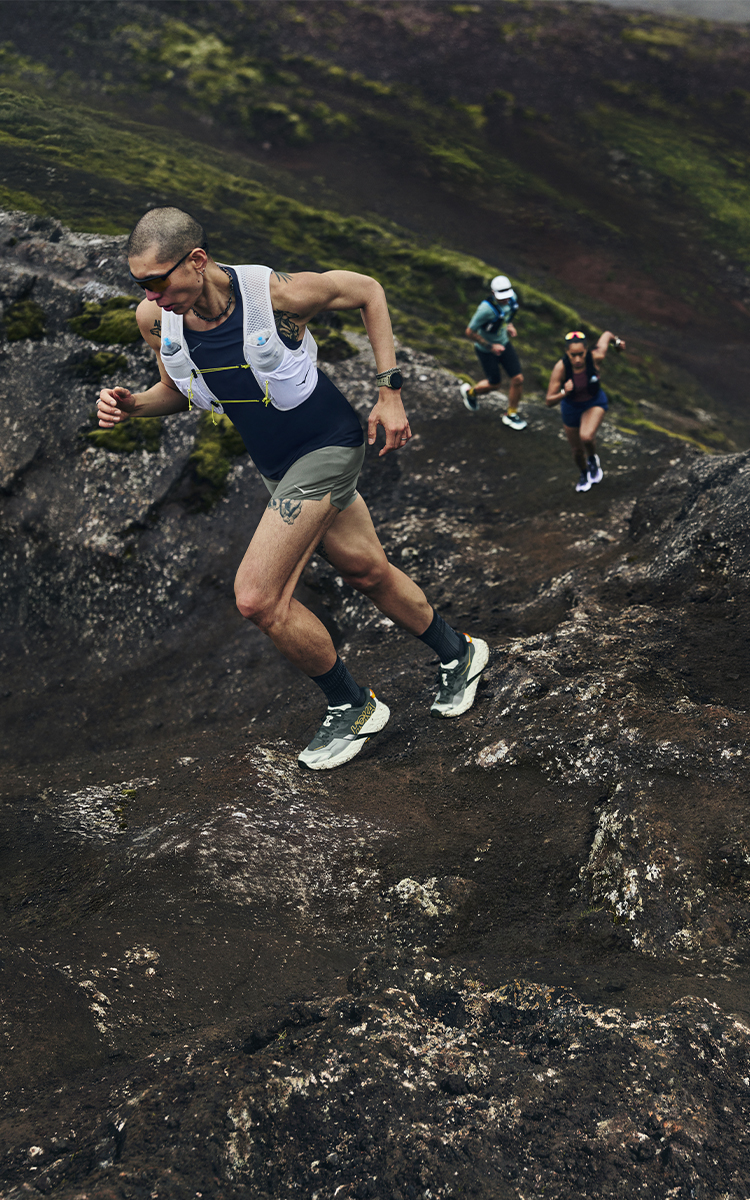 Ragazzo che corre in montagna con scarpe da trail Hoka Speedgoat 7