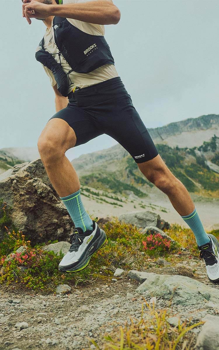 Ragazzo che corre in montagna con scarpe da trail Brooks Cascadia 20