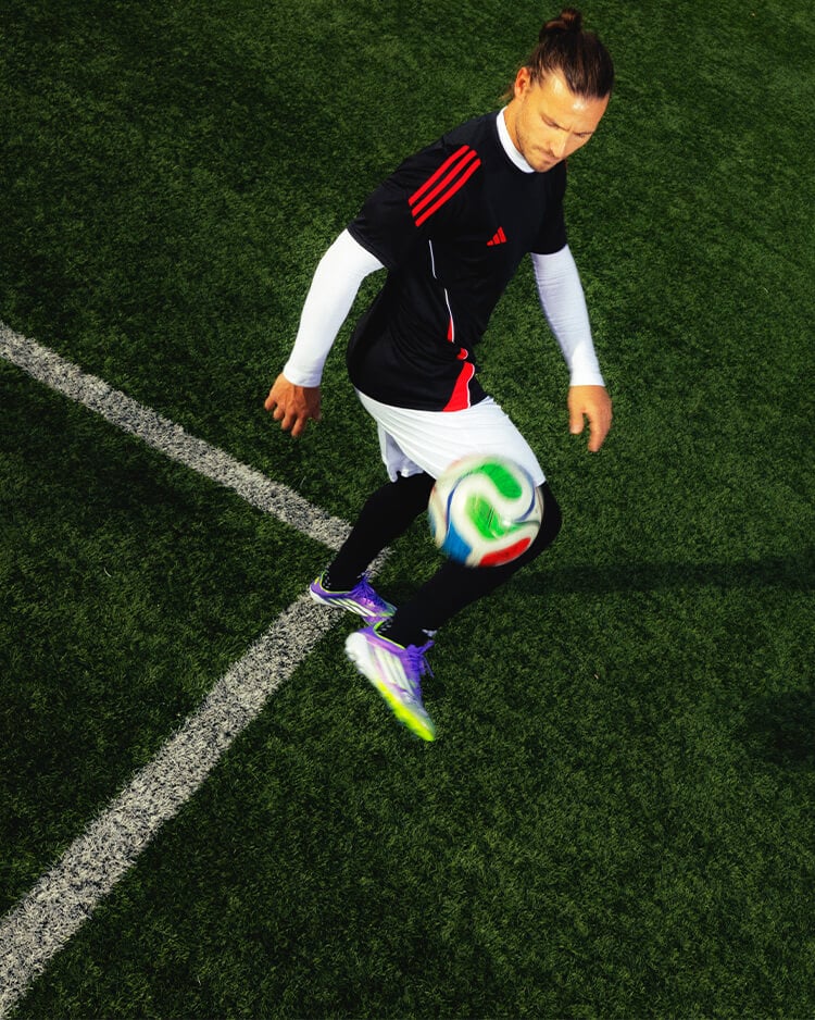 Ragazzo che gioca a calcio in campo, vestito con abbigliamento adidas football