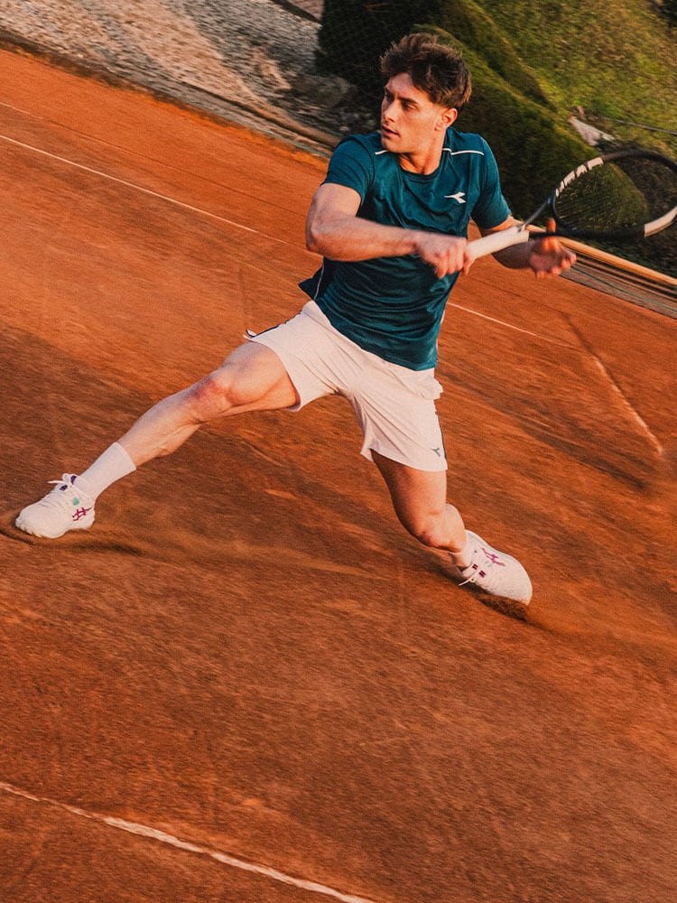 Ragazzo che gioca una partita a tennis su campo rosso