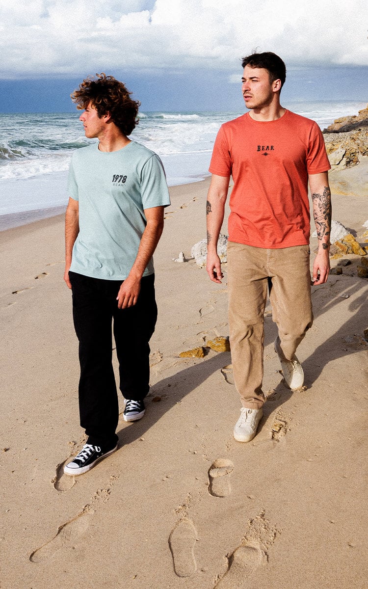 Due ragazzi che camminano in spiaggia vestiti con abbigliamento autunnale firmato Bear Surfboards