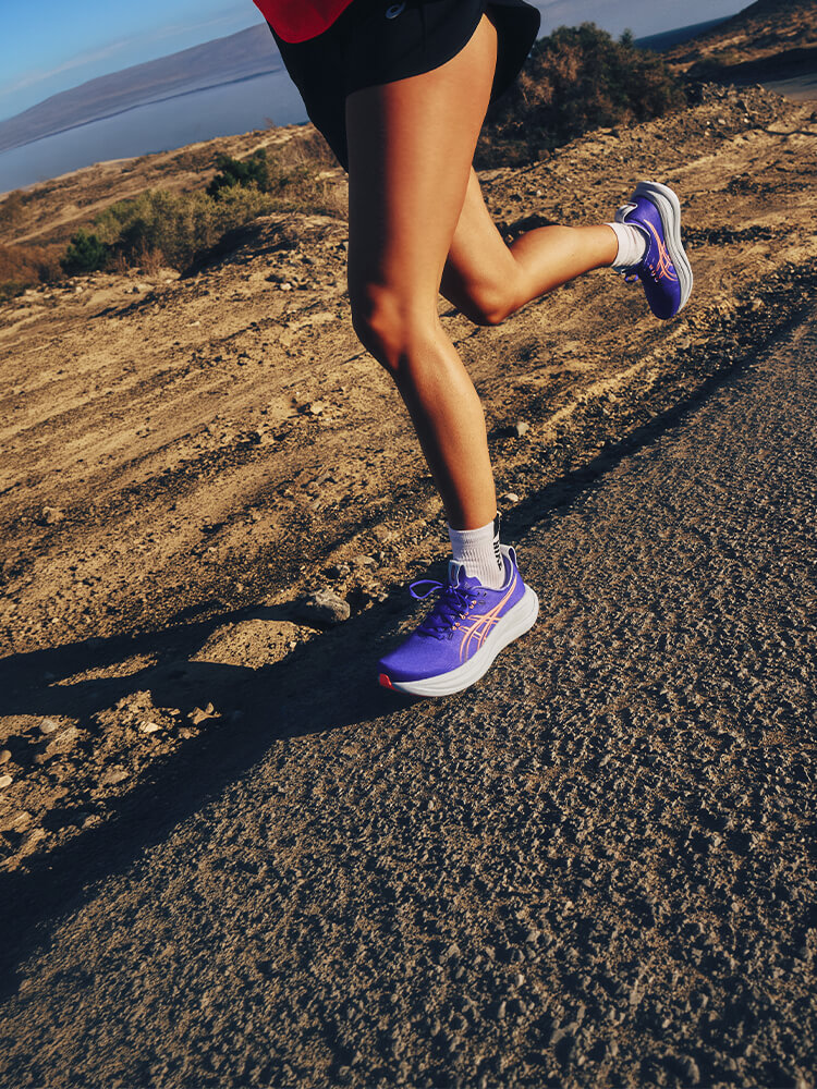 Ragazza che corre in riva al mare. Focus sulle sue scarpe da corsa Asics color viola e rosa
