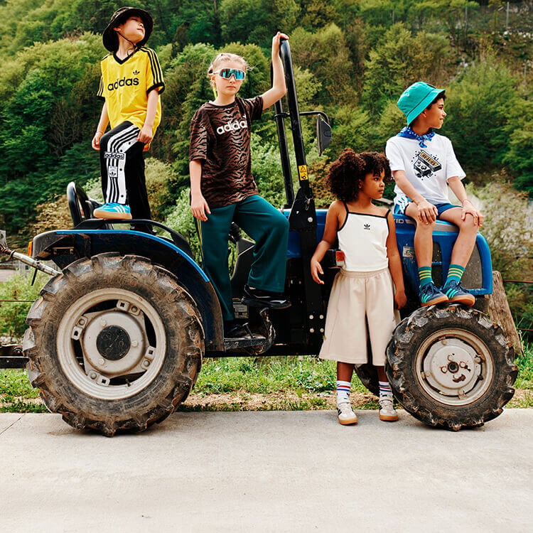 Bambini sopra un trattore che indossano abbigliamento e sneakers adidas