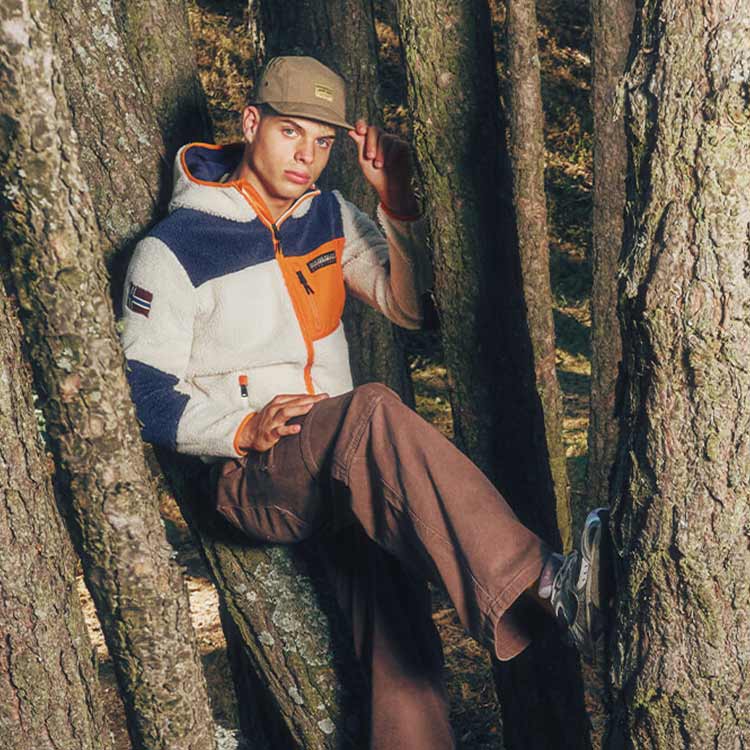 Ragazzo seduto tra degli alberi che indpssa pile Napapijri