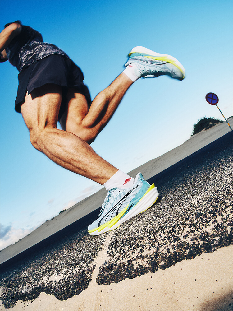 Ragazzo che corre in riva al mare. Focus sulle sue scarpe da corsa Puma azzurre e gialle